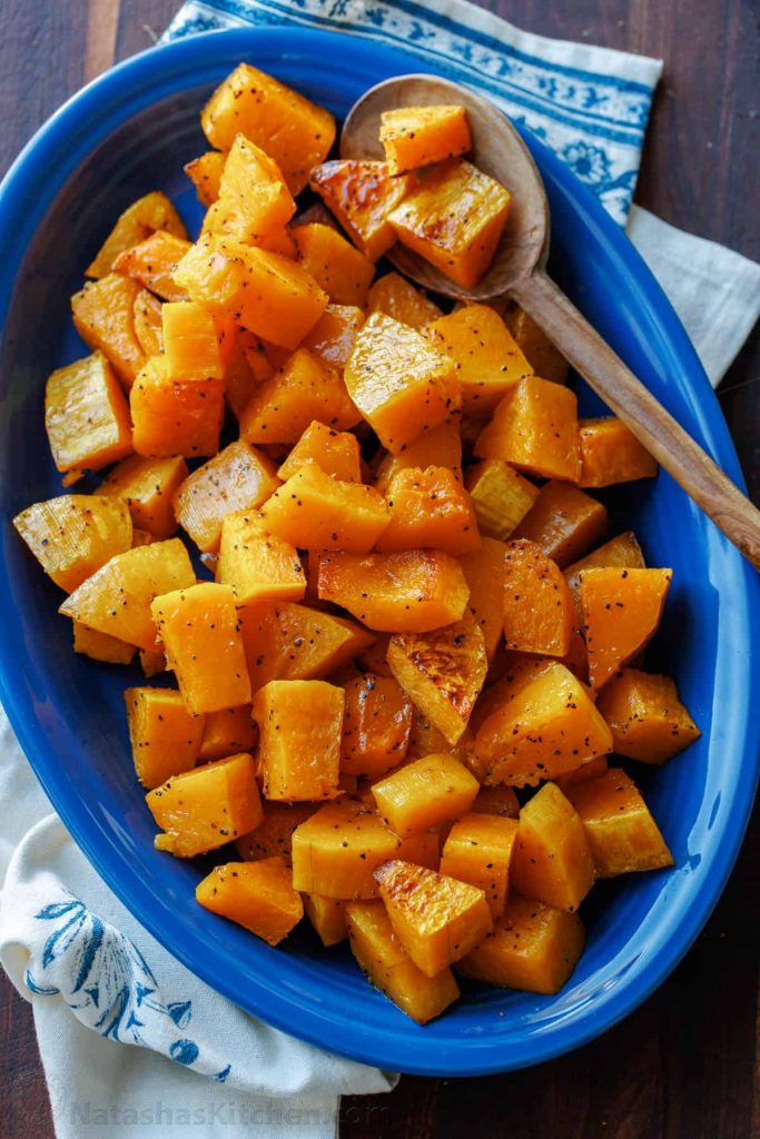 Roasted butternut squash on a blue oval platter with a serving spoon.